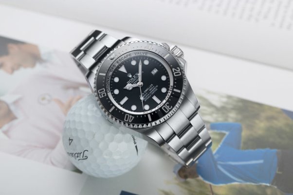 Rolex Deepsea 116660 Edelstahl-Uhr mit schwarzem Zifferblatt auf Golfball und Magazin liegend